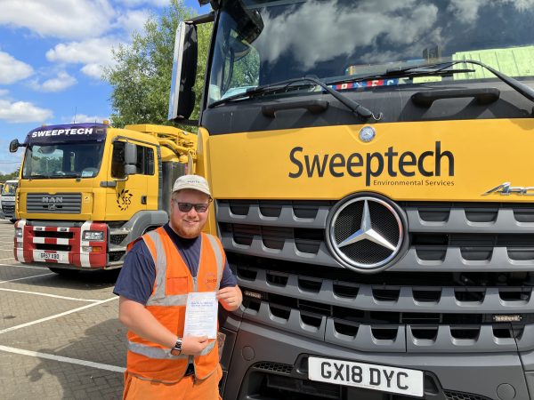 Adam standing in front of a yellow Sweeptech vehicle showing off his HGV Class 2 Licence
